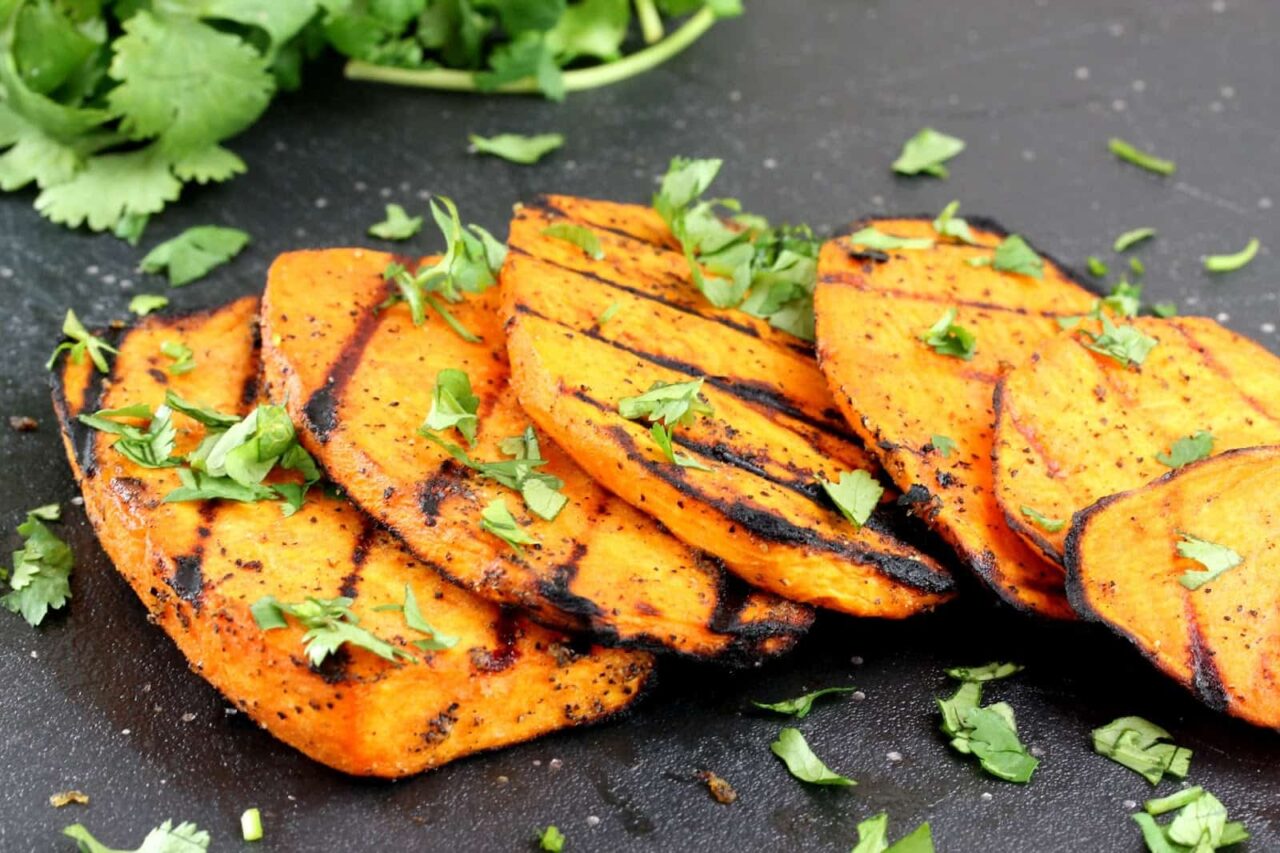 Grilled slices of sweet potatoes on a black cutting board garnished with cilantro