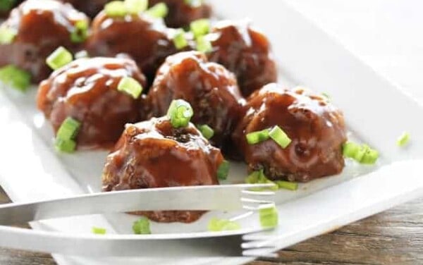 Vegan Sweet and Sour Meatballs on a white serving tray with tongs on it.