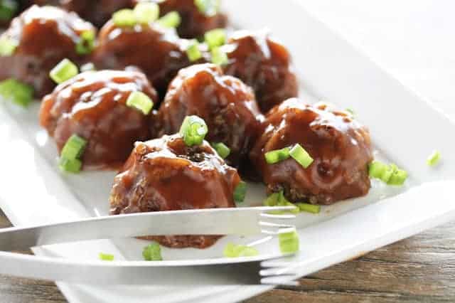 Vegan Sweet and Sour Meatballs on a white serving tray with tongs on it.