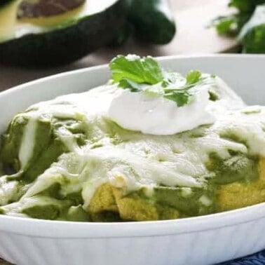 Mole Verde chicken enchiladas in a white dish topped with sour cream and cilantro.