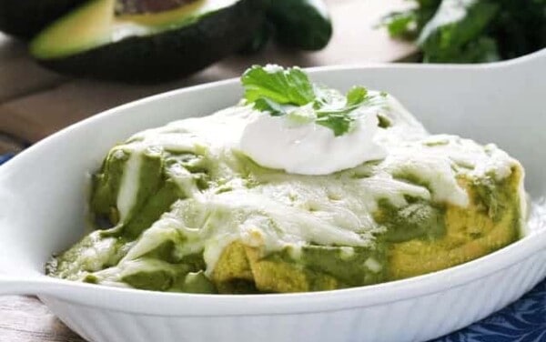 Mole Verde chicken enchiladas in a white dish topped with sour cream and cilantro.