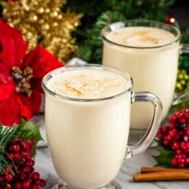 Homemade Eggnog in two mugs surrounded by christmas decorations