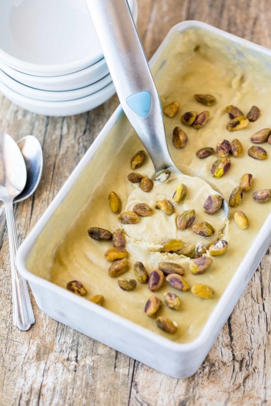 An icecream scoop takes a scoop from a pan of homemade pistachio gelato topped with pistachios