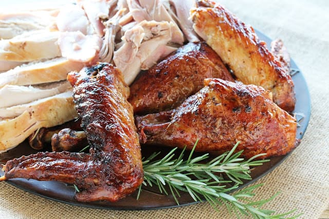 Roasted turkey on a platter with light meat, dark meat and wings and drumsticks with deliciously crispy skin. All garnished with a sprig of rosemary.