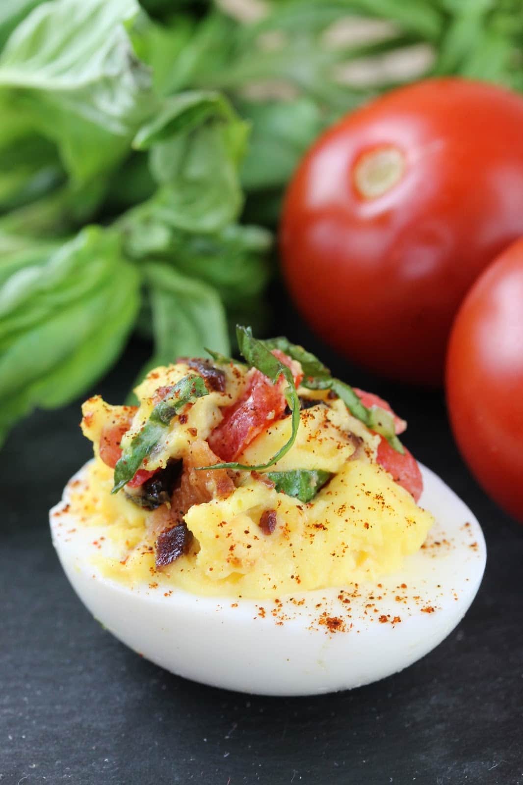 A blt deviled eggs with tomatoes and basil in the background.