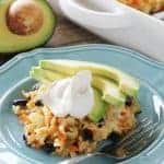 Mexican brown rice and black bean casserole topped with sour cream and avocado slices on a blue plate.