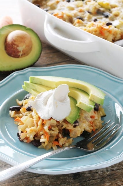 Mexican brown rice and black bean casserole topped with sour cream and avocado slices on a blue plate.