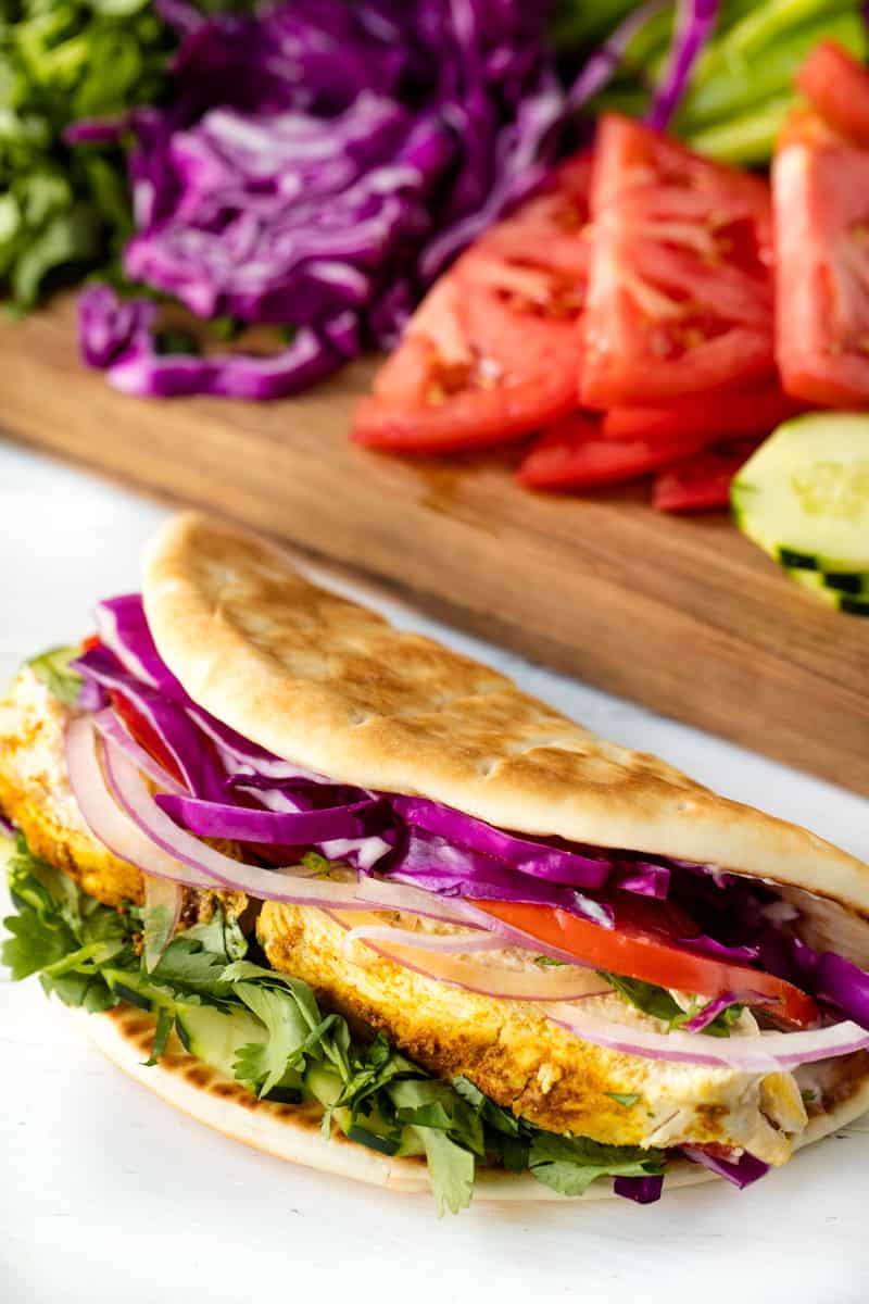 Moroccan Chicken Gyro is sitting on a countertop with a cutting board full of ingredients behind it.