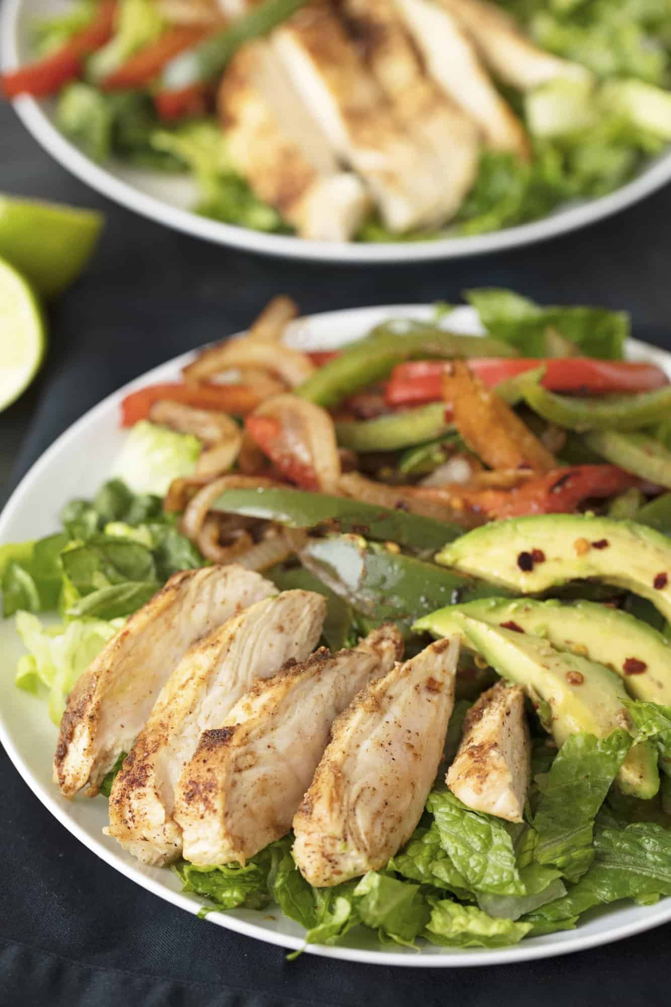 Fajita Salad on a white plate with another salad in the background.