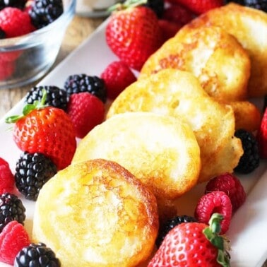 Fried pancakes on a white plate with blackberries and strawberries.