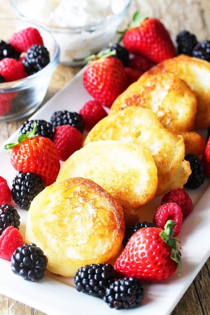 Fried pancakes on a white plate with blackberries and strawberries.