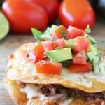 Shredded beef is sandwiched between two crispy fried corn tortillas with plenty of refried beans and cheese. It's topped off with a fresh avocado salsa.
