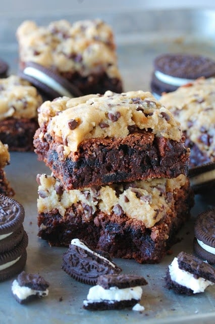 A stack of decadent fudge brownies filled with chunks of Oreo cookies and topped off with raw cookie dough.