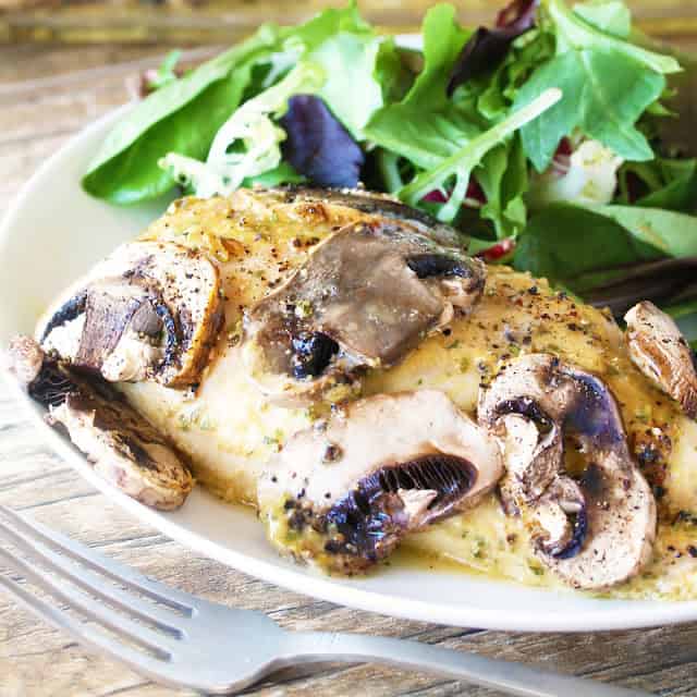 A Baked Honey-Dijon Chicken chicken breast seasoned with tarragon and topped with sliced mushrooms, served with a salad on a plate