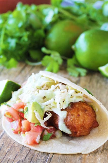 Crispy battered cod is topped with avocado salsa, simple slaw and jalapeno, wrapped in a corn tortilla and served with a lime wedge