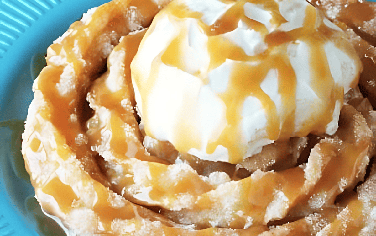 A close up view of a churro funnel cake on a blue plate, topped with whipped cream and drizzled with caramel sauce.