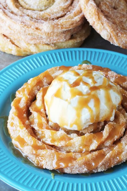 A churro funnel cake topped with whipped cream and caramel sauce on a blue plate.