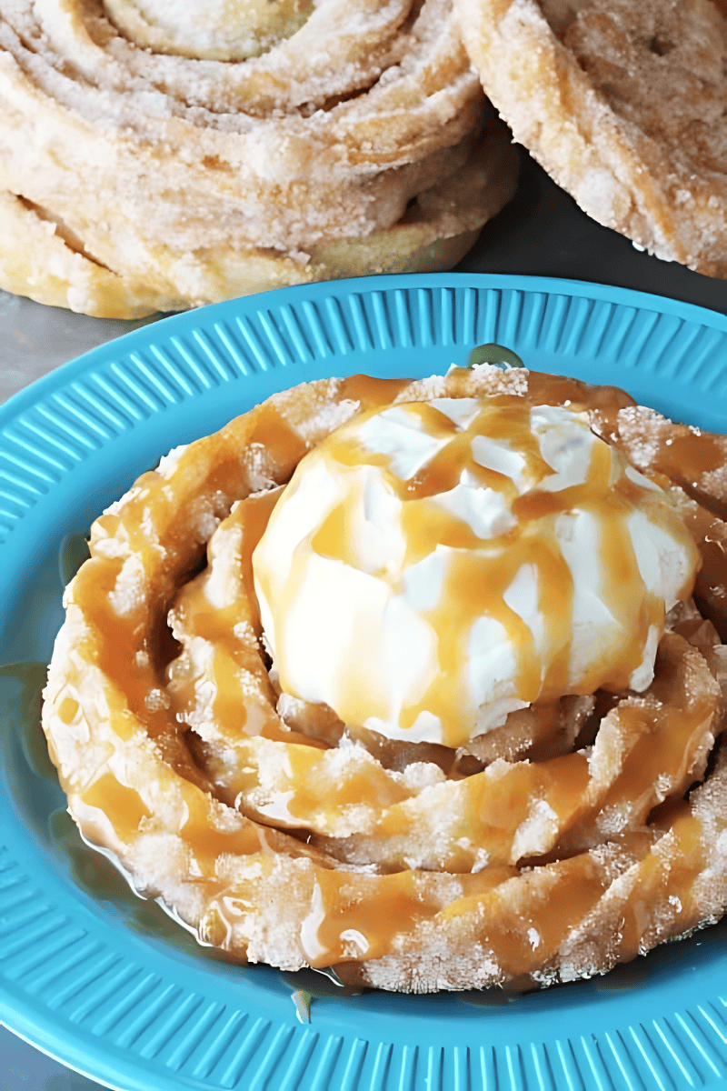 A churro funnel cake on a blue plate, topped with whipped cream and drizzled with caramel sauce.