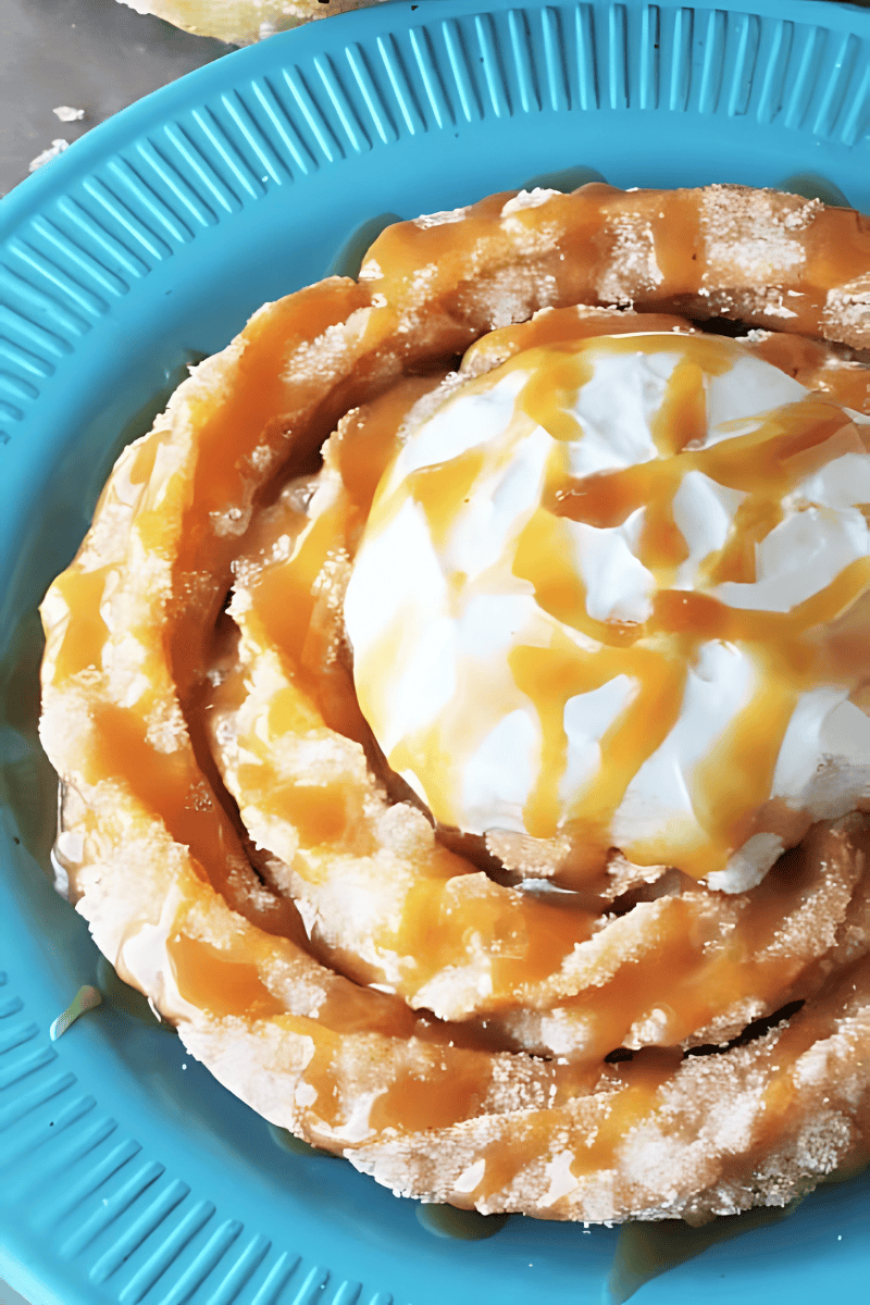 An overhead view of a churro funnel cake on a blue plate, topped with whipped cream and drizzled with caramel sauce.