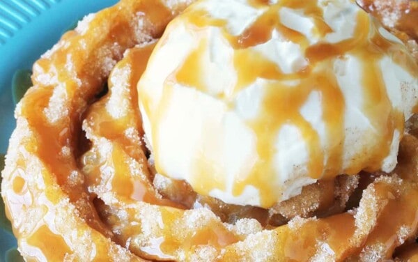 Close-up view of Churro Funnel Cake on teal dish topped with vanilla ice cream and drizzled with caramel syrup.