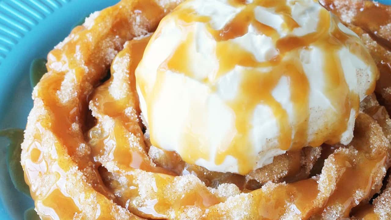 Close-up view of Churro Funnel Cake on teal dish topped with vanilla ice cream and drizzled with caramel syrup.