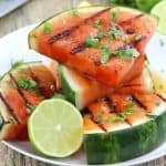 Grilled sliced watermelon with cilantro and lime wedges on a white plate
