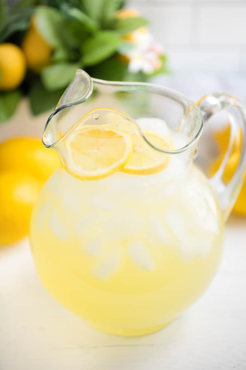 Glass pitcher full of lemonade, ice, and lemon slices.