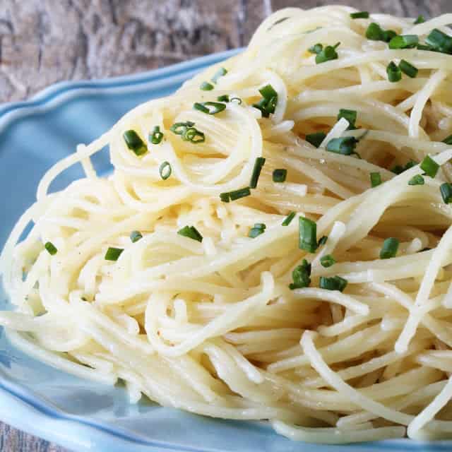 Nutty brown butter is infused with garlic to flavor this Brown Butter Garlic Angel Hair Pasta. Tossed with freshly grated parmesan, topped with fresh chopped chives and served on a blue plate.