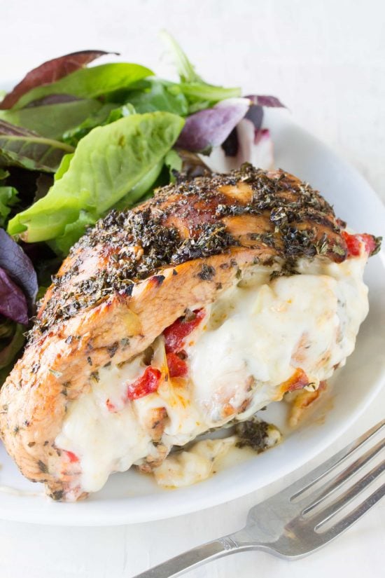 Italian Stuffed Chicken: Balsamic and herb glazed chicken, stuffed with artichoke, bell pepper, and fennel and oozing with melted mozzarella, served with a salad on a plate.