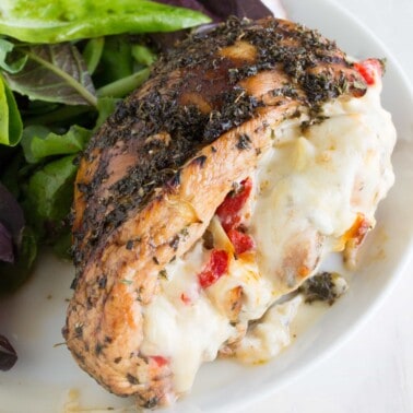 Italian Stuffed Chicken: Balsamic and herb glazed chicken, stuffed with artichoke, bell pepper, and fennel and oozing with melted mozzarella, served with a salad on a plate.