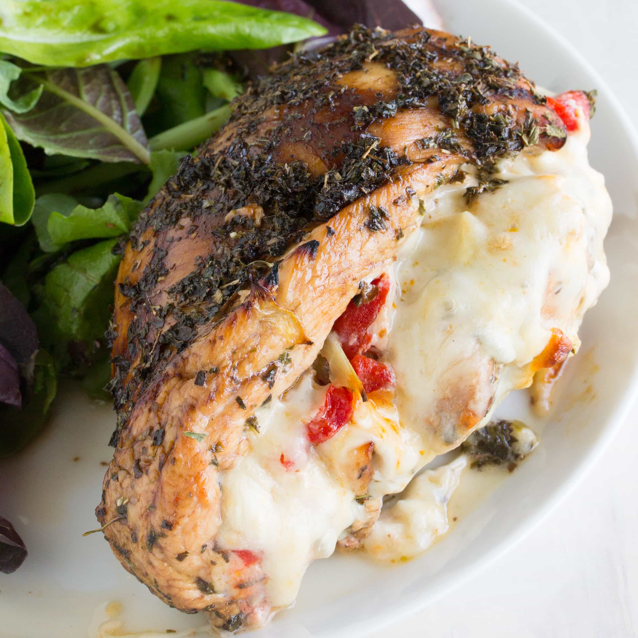 Italian Stuffed Chicken: Balsamic and herb glazed chicken, stuffed with artichoke, bell pepper, and fennel and oozing with melted mozzarella, served with a salad on a plate.