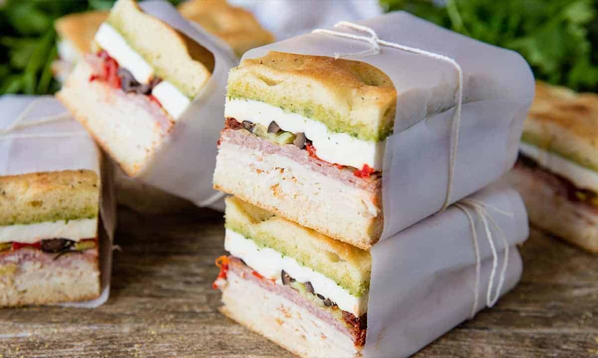 Stacked Clean Cut Pressed Italian Sandwiches with cold cuts and fillings wrapped in parchment paper