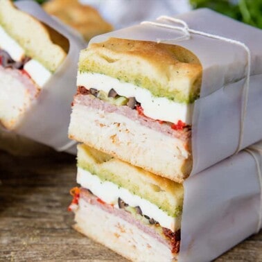 Stacked Clean Cut Pressed Italian Sandwiches with cold cuts and fillings wrapped in parchment paper