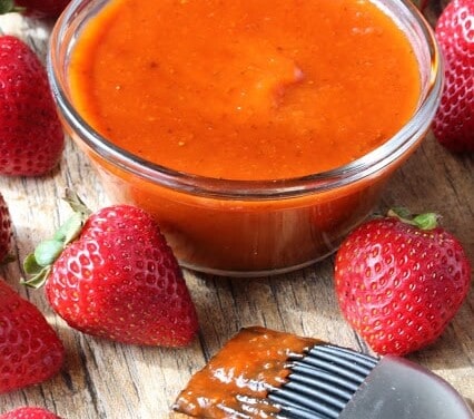 Glass bowl of strawberry chipotle BBQ sauce surrounded by strawberries.