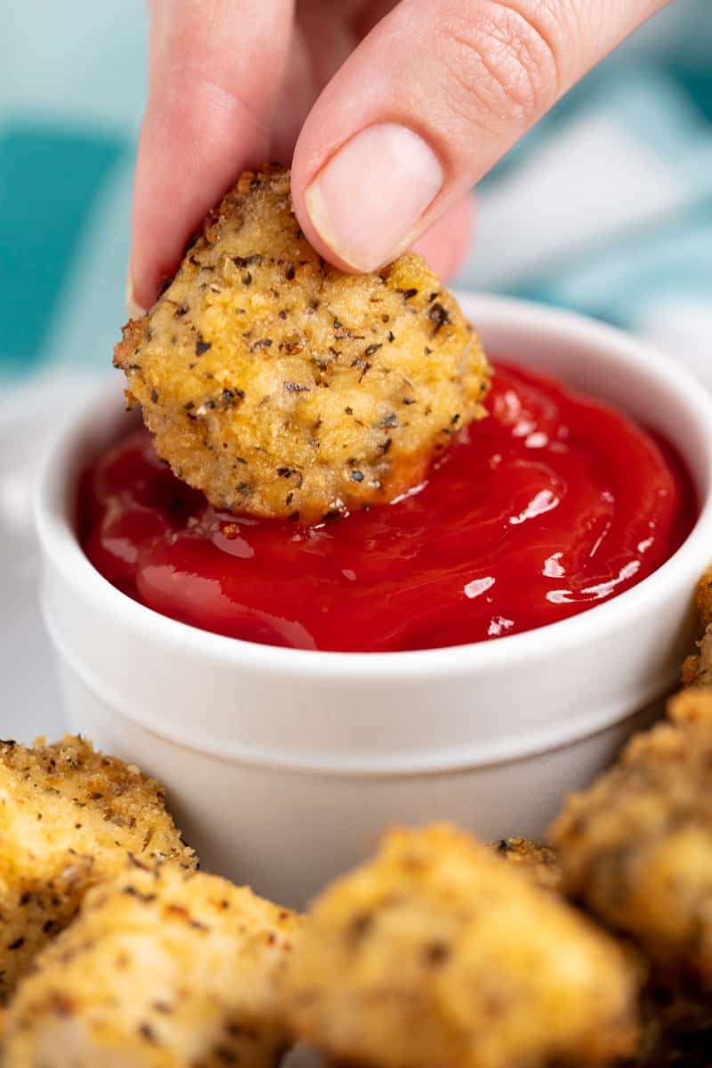 baked chicken nuggets being dunked into ketchup