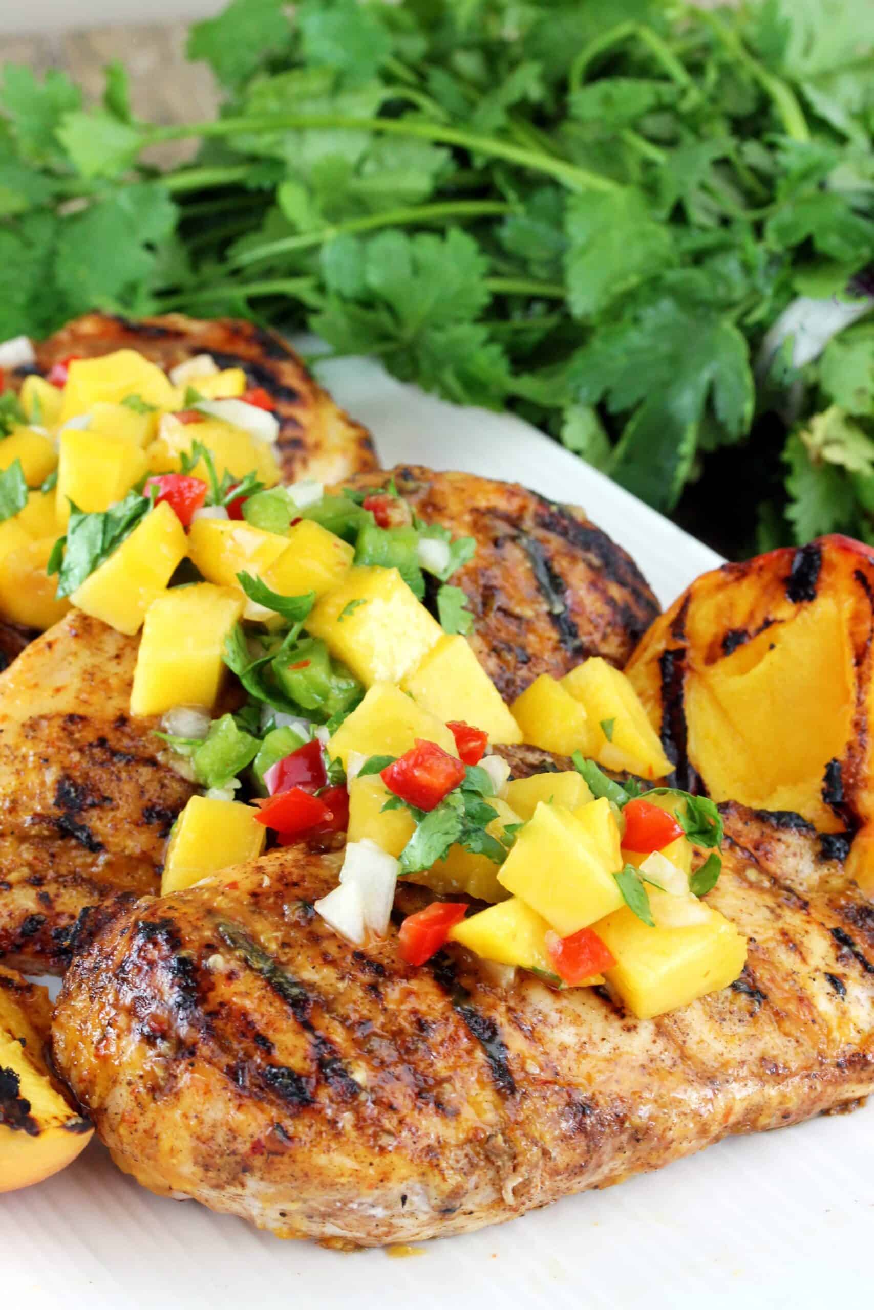 Chipotle-Peach Glazed Grilled chicken breasts on a plate is topped with peach salsa, cilantro in background