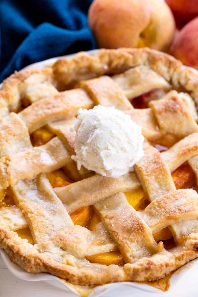 Peach Pie in a ceramic pie pan topped with a scoop of ice cream.