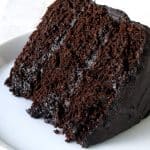 A slice of Moist Chocolate Cake layered with chocolate frosting with a bite taken out with a fork