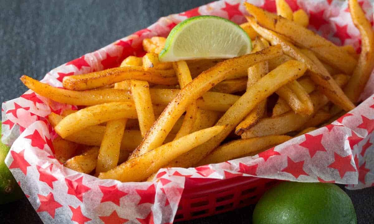 Angled view of Baked Chili-Lime French Fries served in a diner basket and garnished with lime wedges.