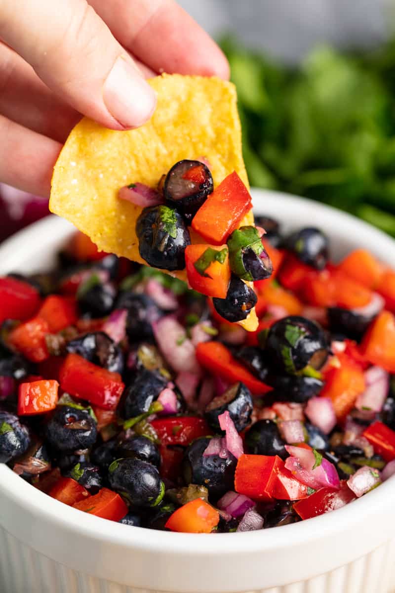 A chip dips into a bowl of Blueberry Red Bell Pepper Salsa