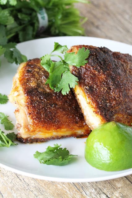 Chicken Thighs and half a lime on a white plate.