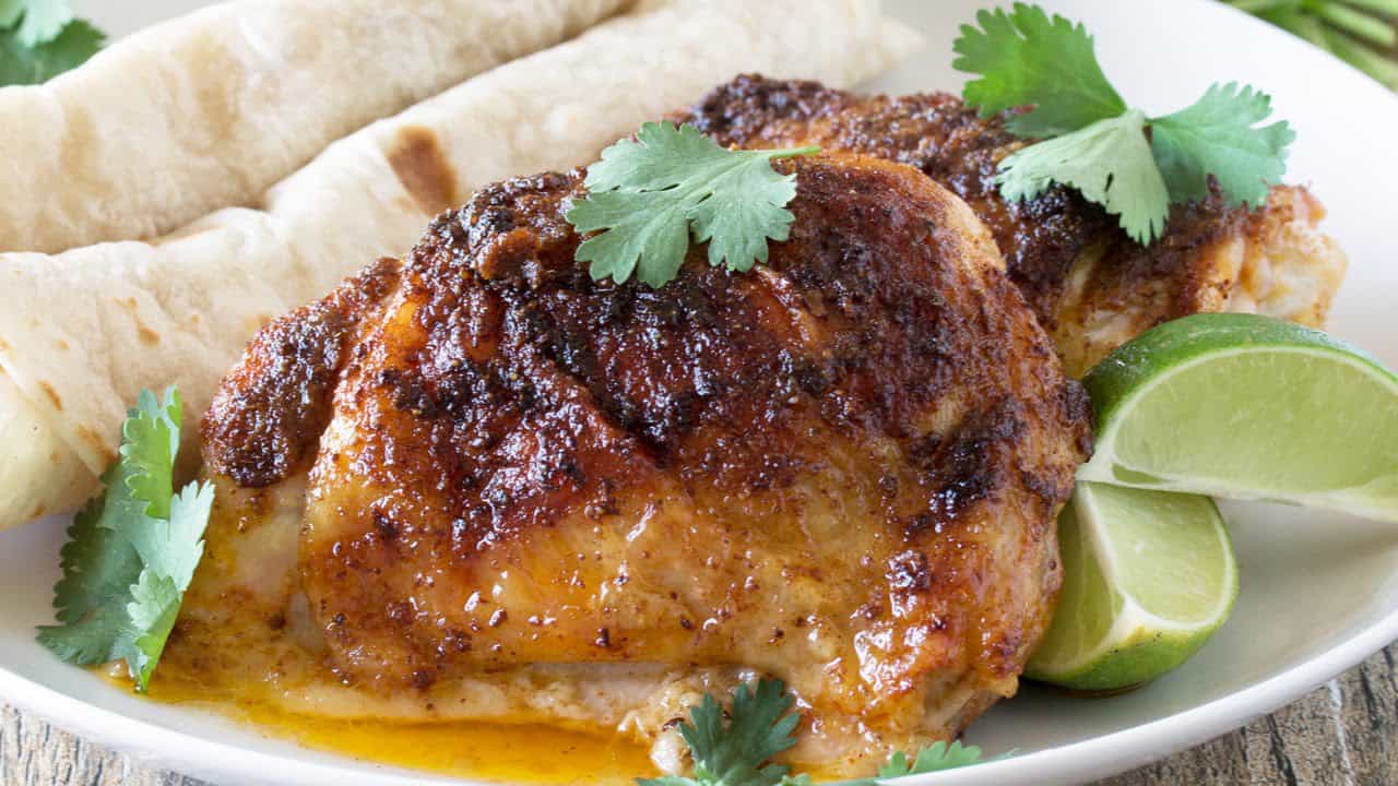 Angled view of Mexican-Spiced Chicken Thighs served up with warm tortillas garnished with lime wedges and parsley.