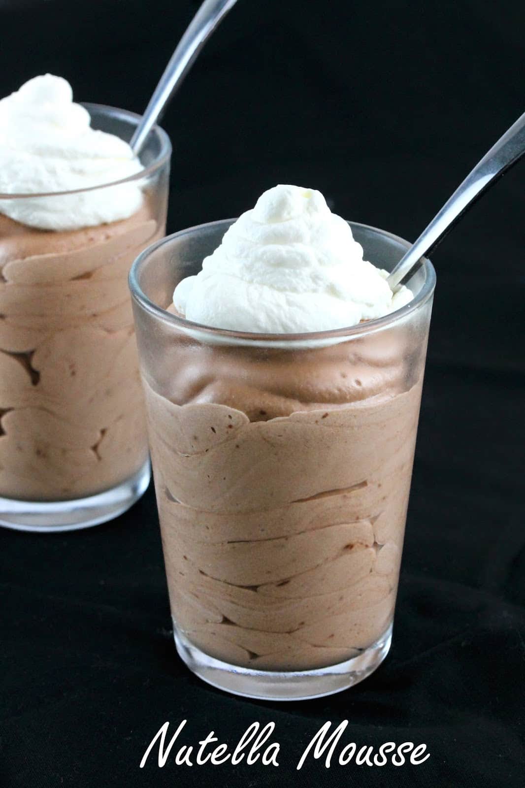 Nutella mousse topped with whipped cream in a glass with a spoon in it.