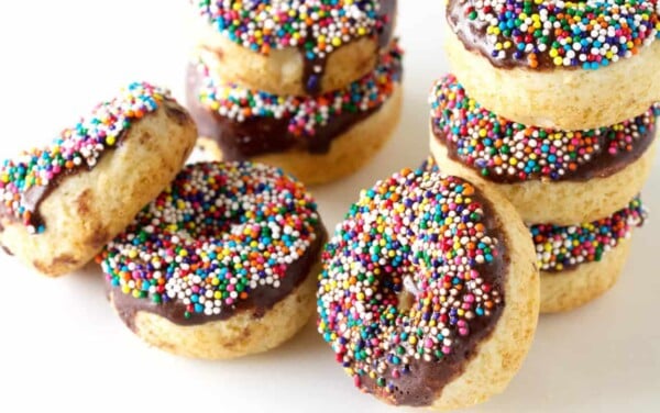 Angled view of stacked baked vanilla cake donuts topped with a semi-sweet chocolate glaze and sprinkles.