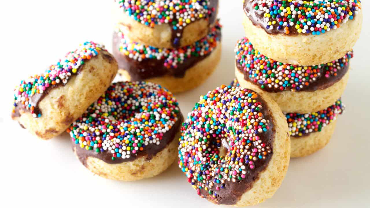 Angled view of stacked baked vanilla cake donuts topped with a semi-sweet chocolate glaze and sprinkles.