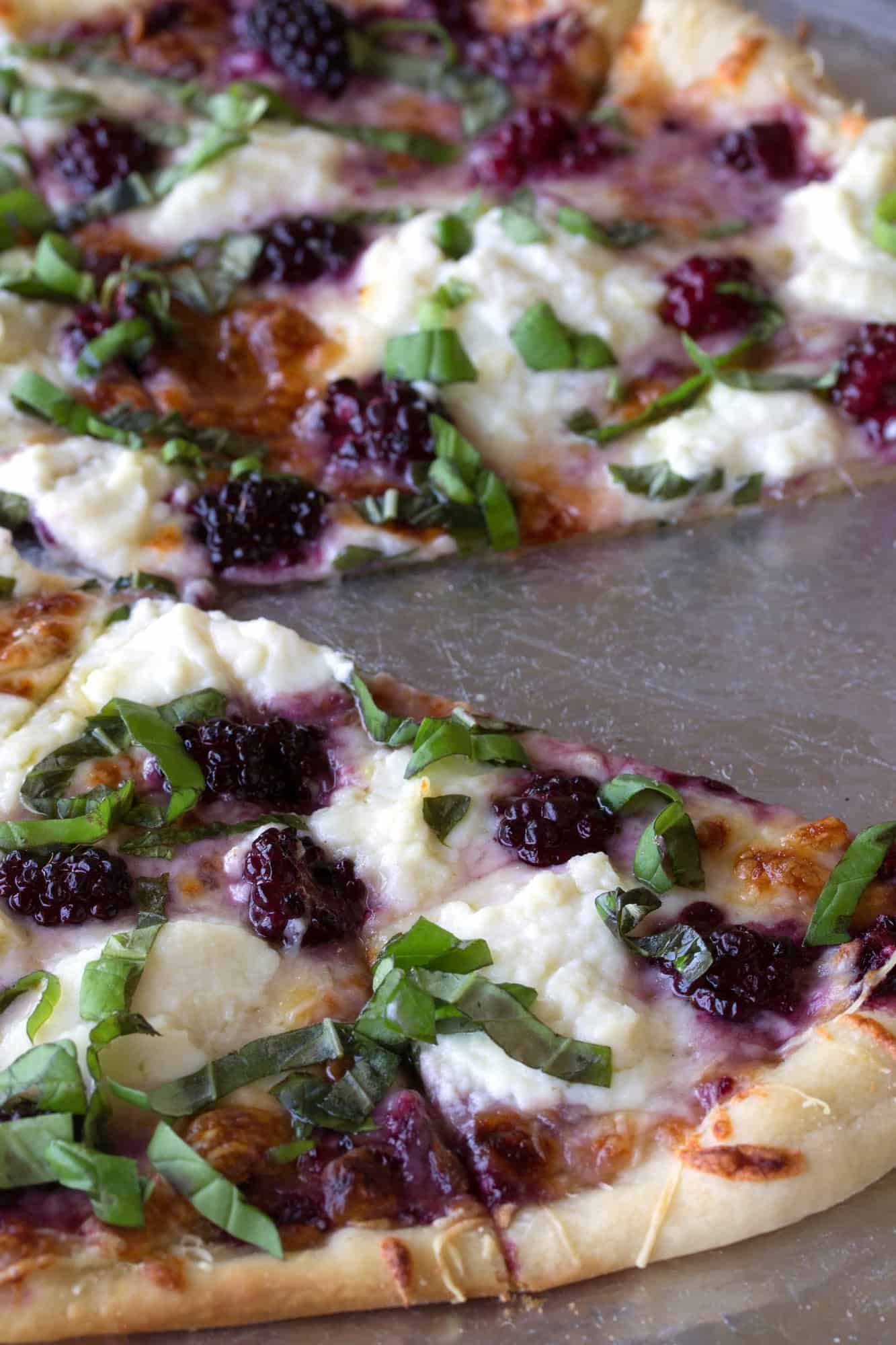 blackberry basil ricotta pizza on a pizza tray with a slice missing.