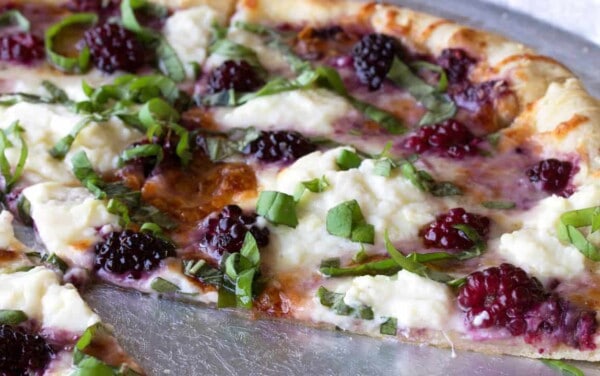 Angled view of Blackberry Basil Ricotta Pizza cut on a silver pizza plate garnished with green onion and ready to eat.