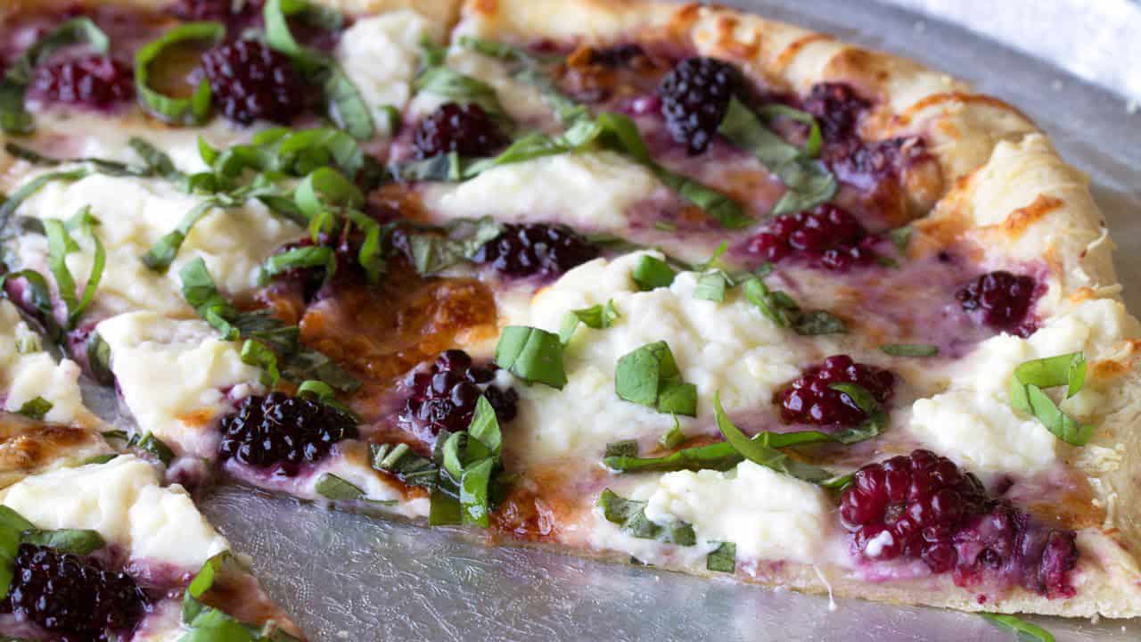 Angled view of Blackberry Basil Ricotta Pizza cut on a silver pizza plate garnished with green onion and ready to eat.
