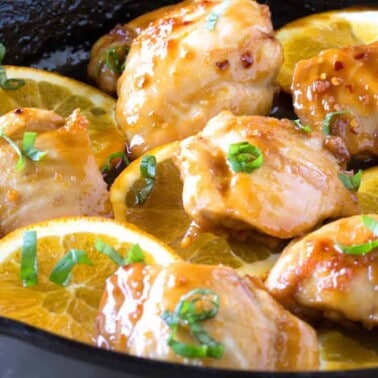 Angled view of moist and juicy chicken thighs in an Asian-inspired orange glaze sizzling in a cast iron skillet.