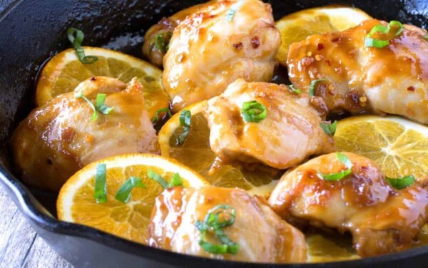 Angled view of moist and juicy chicken thighs in an Asian-inspired orange glaze sizzling in a cast iron skillet.